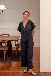 Woman in a charcoal linen outfit standing in a room with wooden flooring and a table.